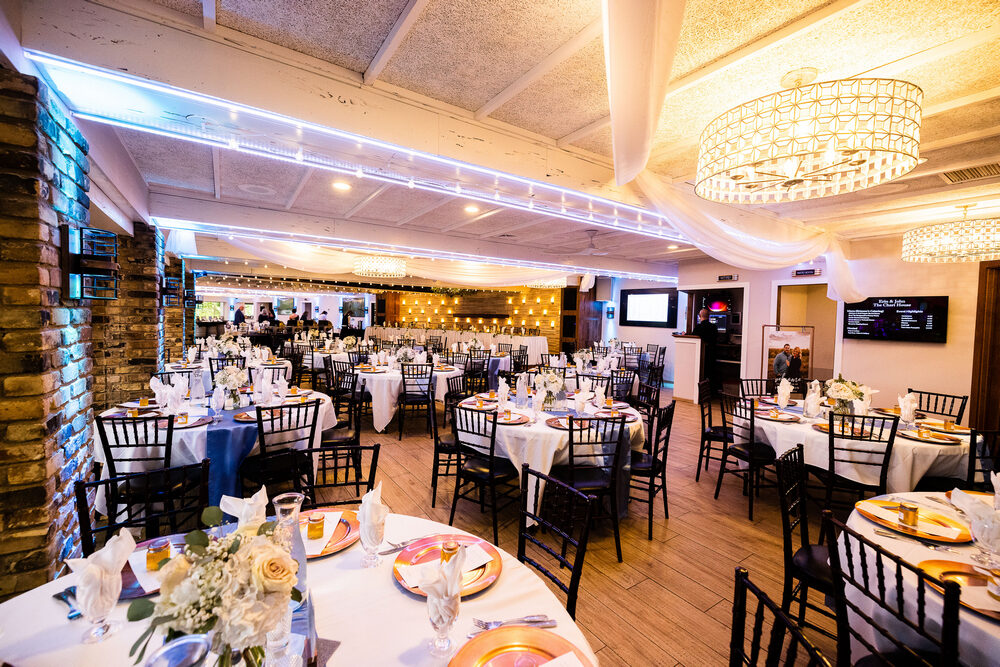 Kingsley Ballroom set with round tables, gold chargers, and blue uplighting along the exposed brick wall at The Chart House, Lakeville MN