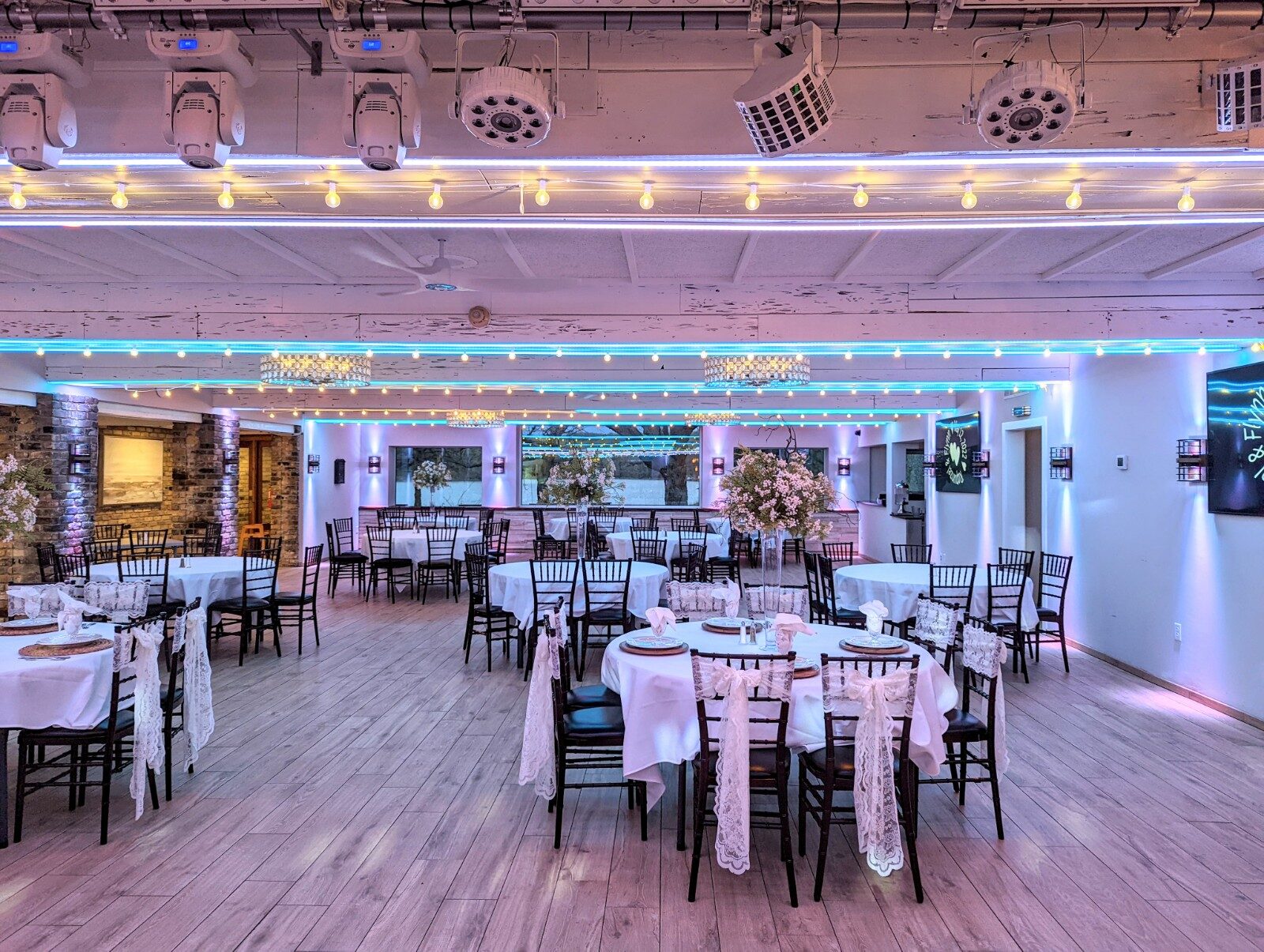 Reception tables dressed with lace chair sashes under teal and pink uplighting in the ballroom at The Chart House, Lakeville MN