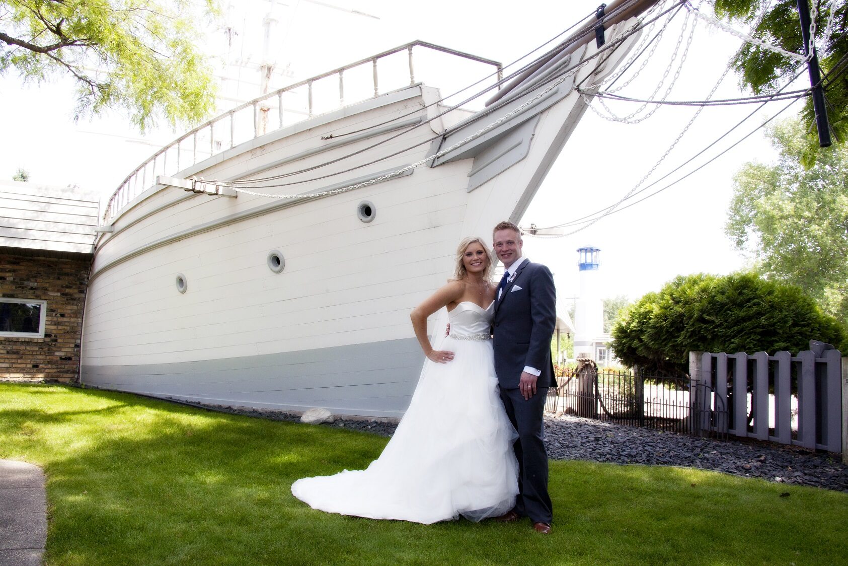 Bride and groom pose beside the landmark white ship and lighthouse on the grounds at The Chart House, Lakeville MN