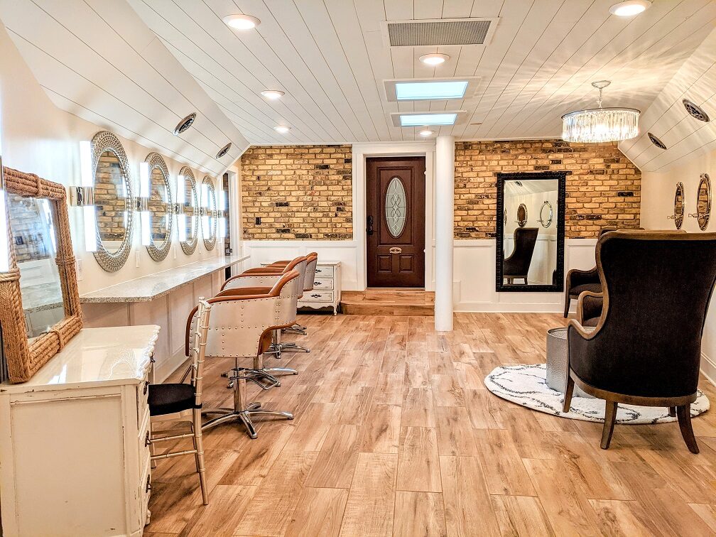 Bridal salon getting-ready suite with styling chairs, lit vanity mirrors, and an exposed brick wall at The Chart House in Lakeville, Minnesota