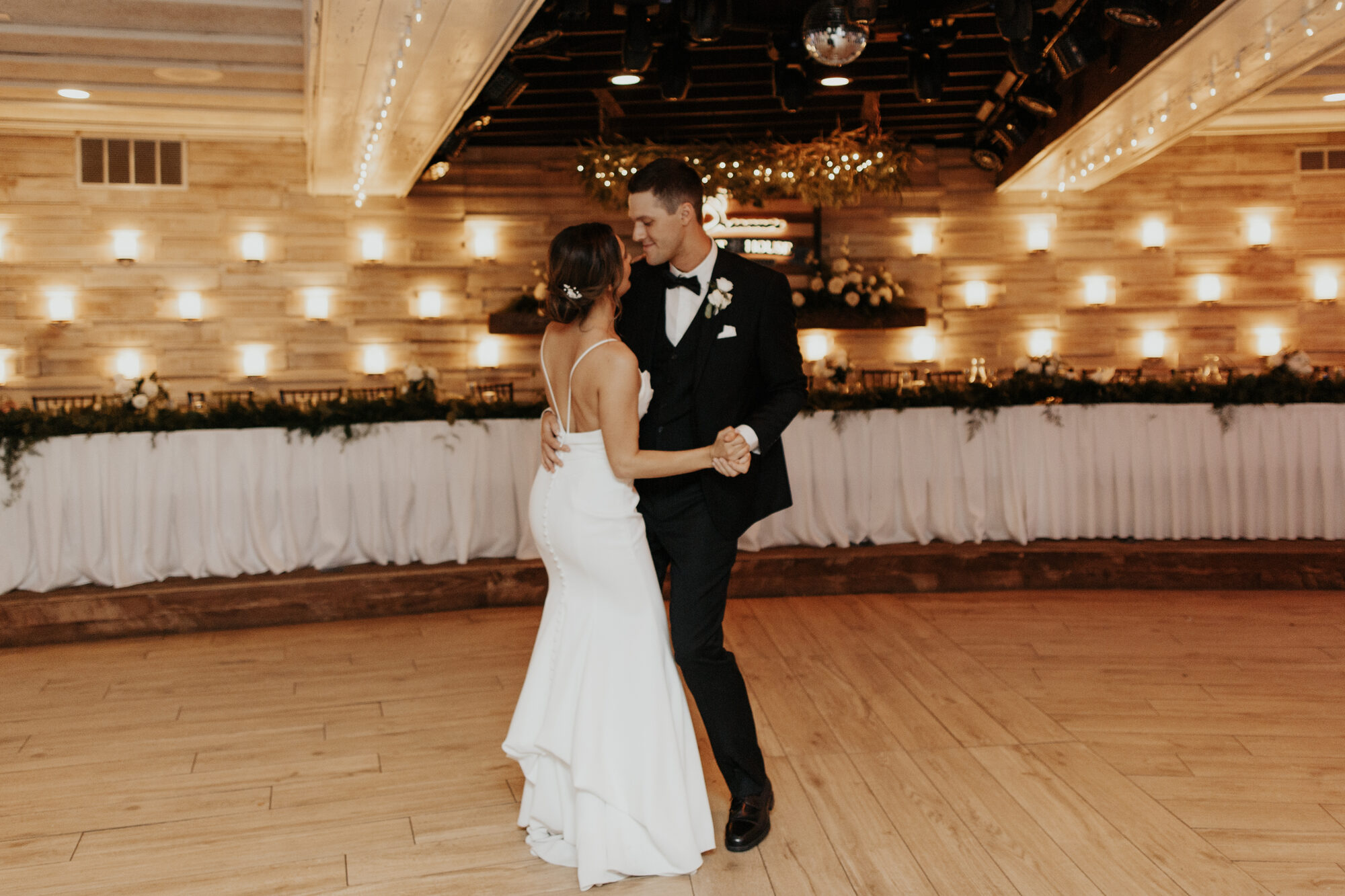 Newlyweds dancing on the wood floor beneath string lights in the Kingsley Ballroom at The Chart House, Lakeville MN