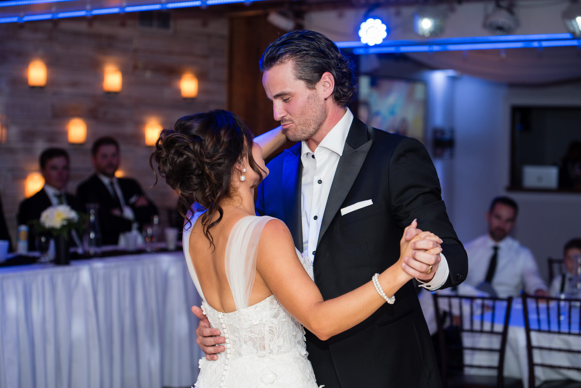 Bride and groom dance closely under blue uplighting as guests watch from the head table at The Chart House, Lakeville MN