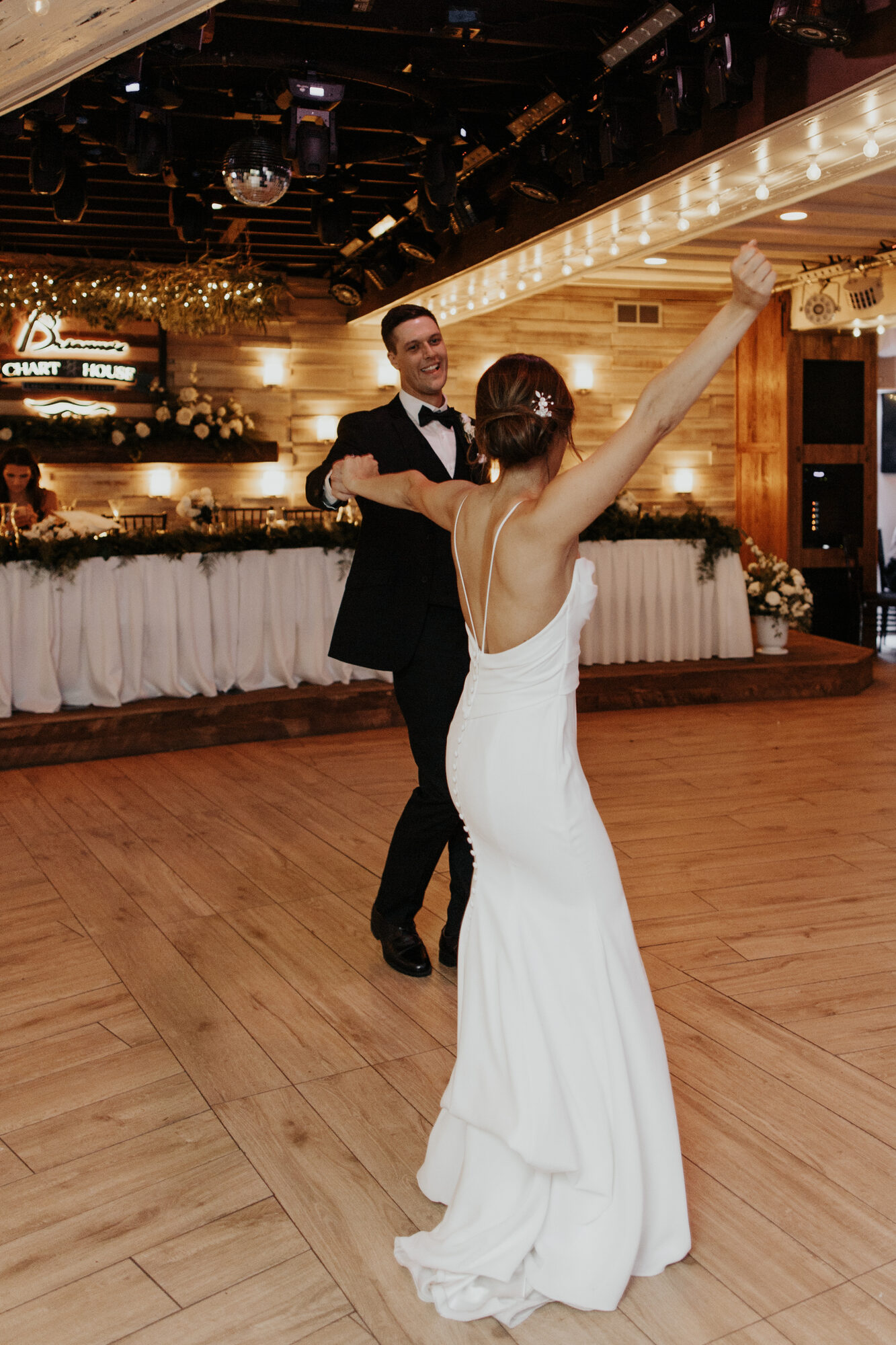Bride raises her arm in celebration during the first dance by the Brianno's Chart House sign in Lakeville MN