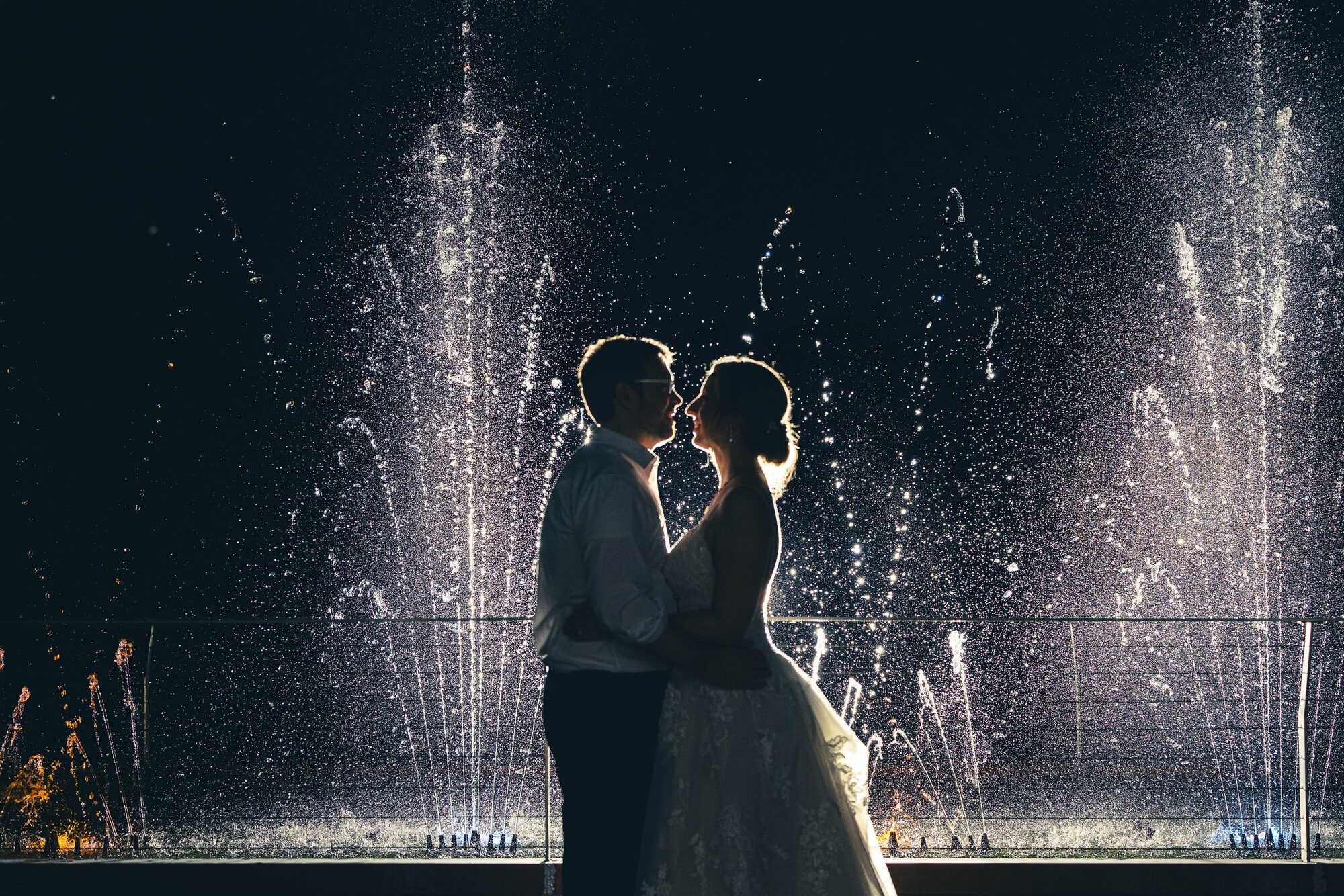 Bride and groom silhouetted against an illuminated fountain at night at The Chart House, Lakeville MN