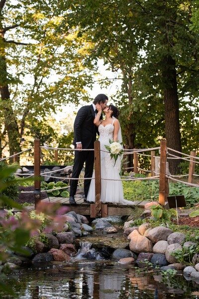 Couple kiss on the rope bridge over the koi stream in the gardens at The Chart House, Lakeville MN
