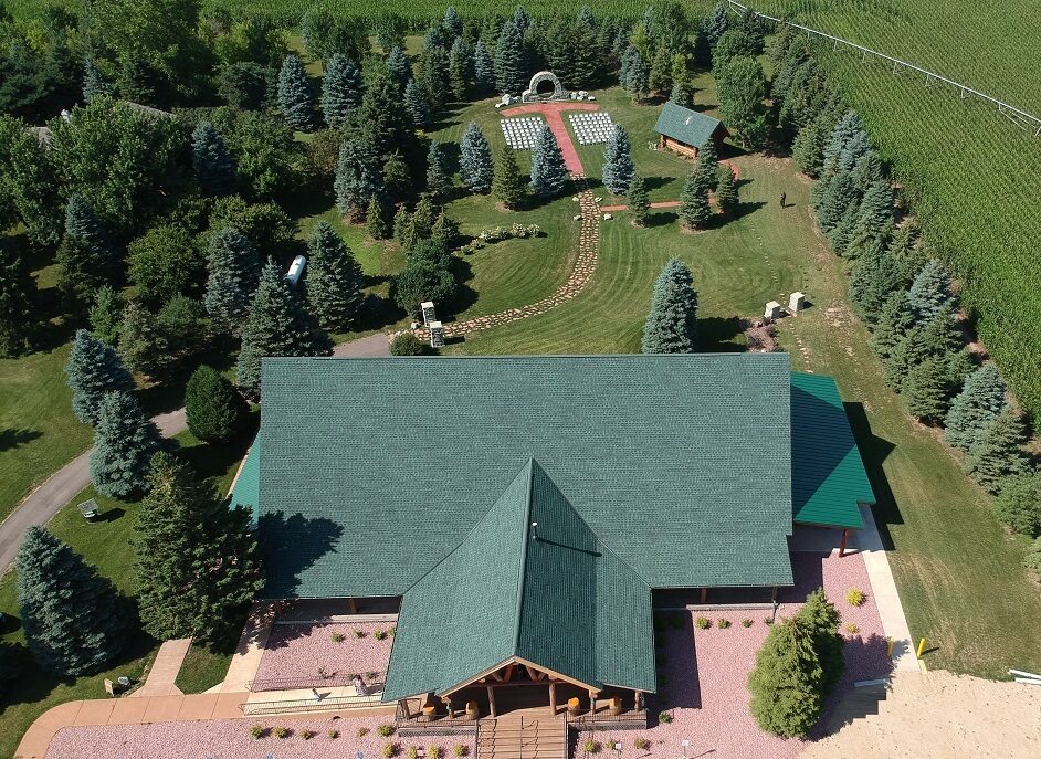 Aerial view of the Glenhaven Events log lodge surrounded by evergreens with the outdoor ceremony arch in Farmington, Minnesota