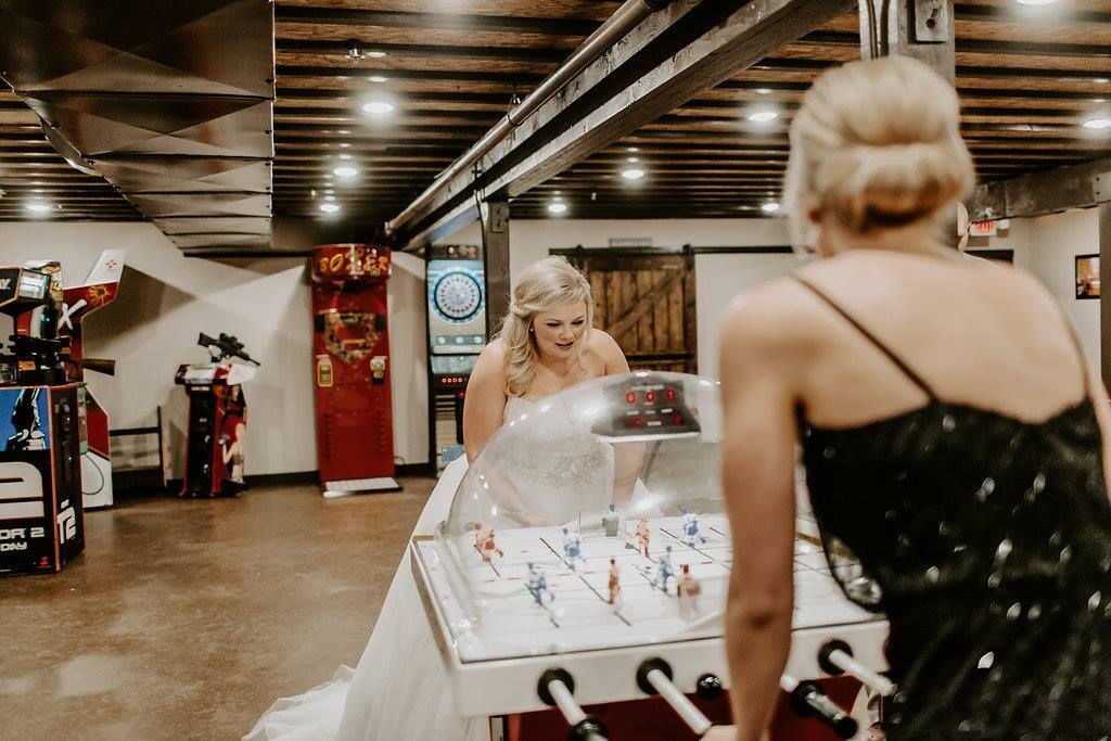 Bride playing bubble hockey in the arcade game room with classic arcade cabinets at Glenhaven Events, Farmington MN