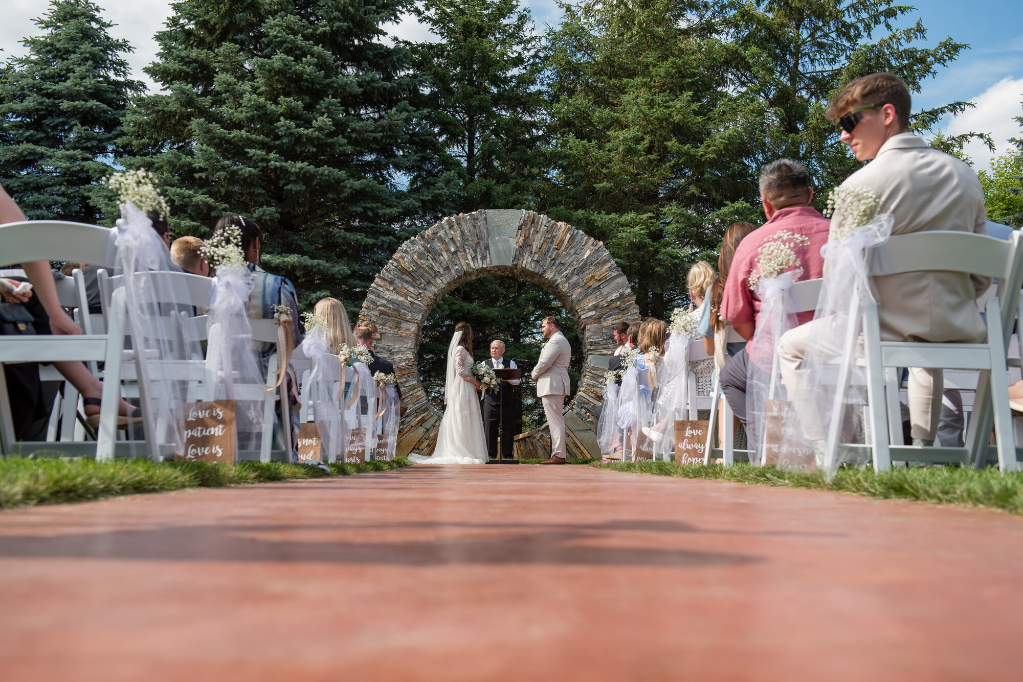 Bride and groom exchange vows beneath the stone moon-gate arch as guests look on at Glenhaven Events, Farmington MN