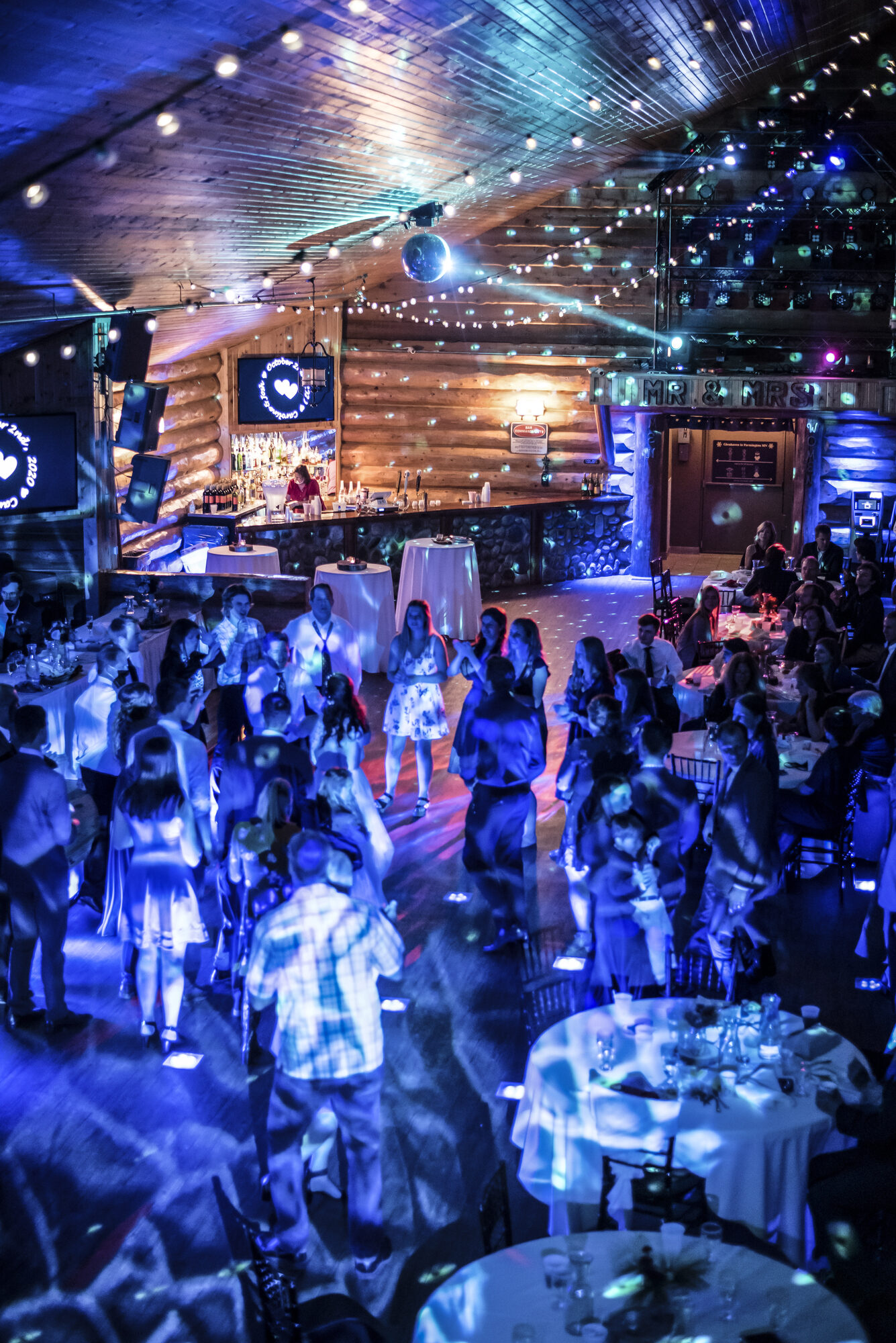 Packed dance floor under a disco ball and blue lighting in the log lodge at Glenhaven Events, Farmington MN