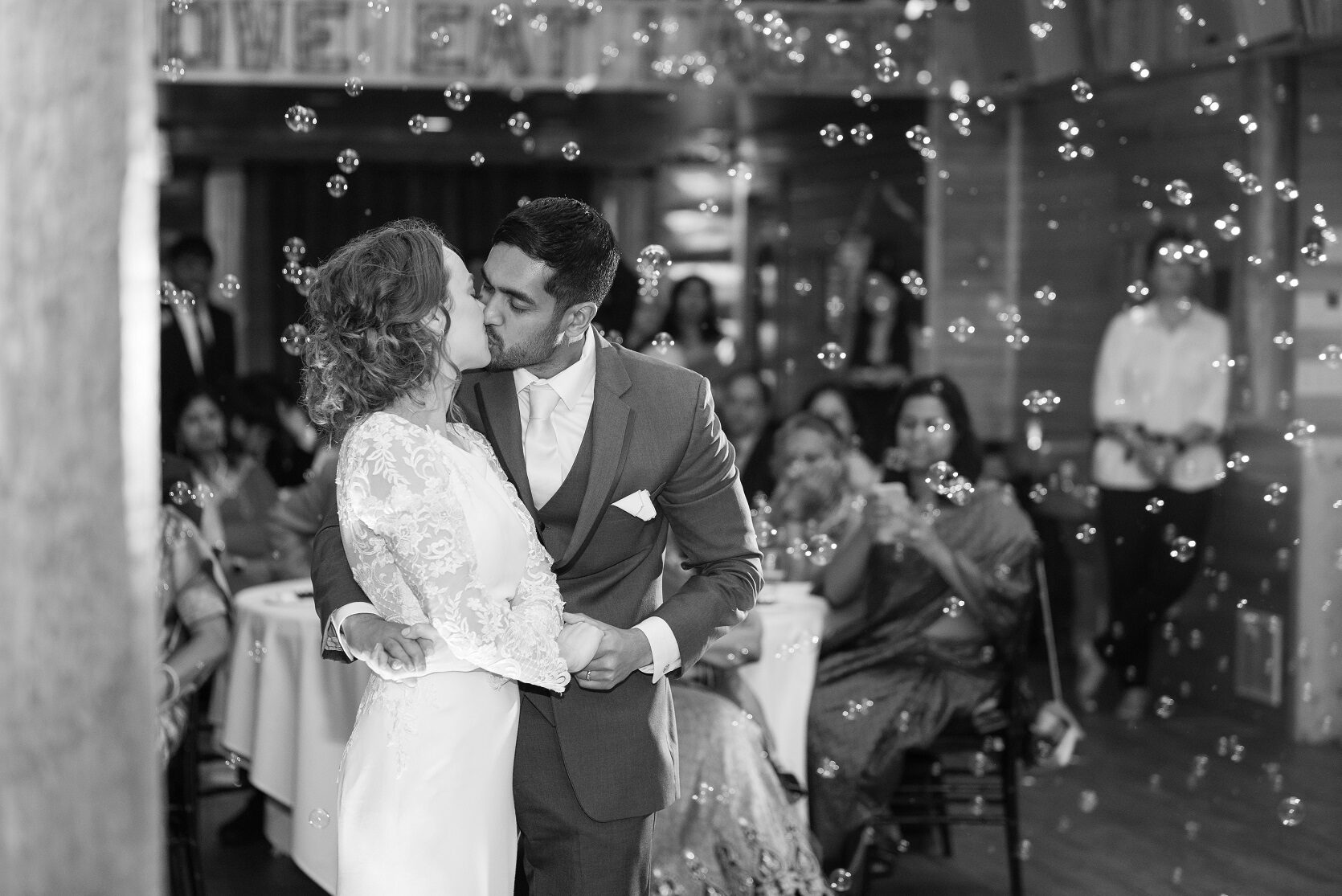 Black and white photo of newlyweds kissing during their first dance amid floating bubbles at Glenhaven Events, Farmington MN