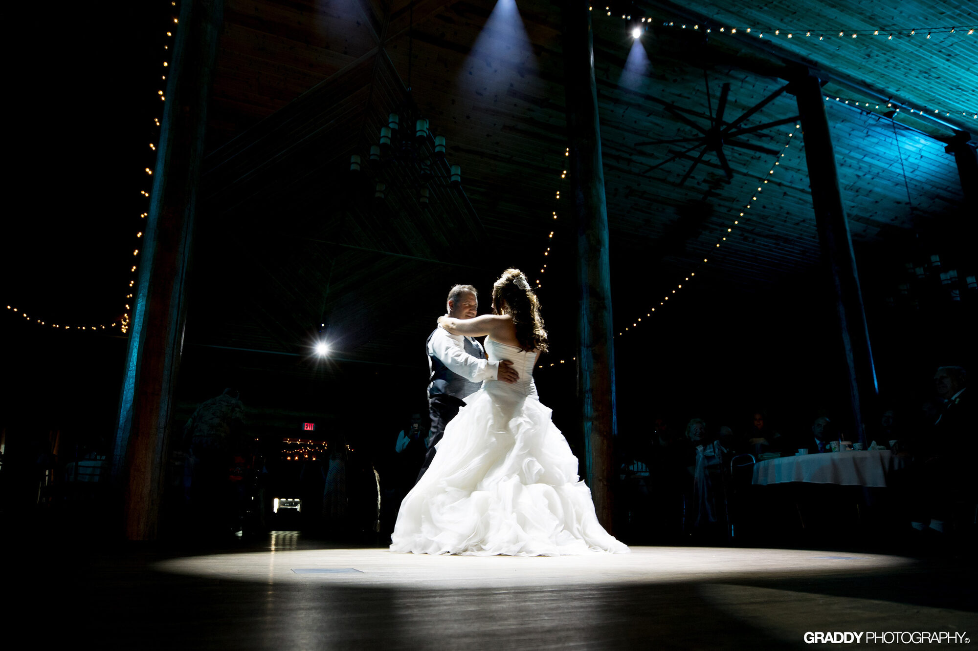 Bride and groom dance in a spotlight beneath the string-lit timber ceiling at Glenhaven Events, Farmington MN