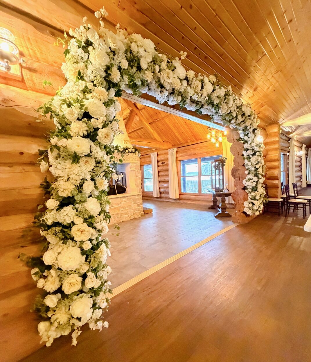 White floral arch overflowing with roses and hydrangea framing the log-walled ceremony space at Glenhaven Events, Farmington MN