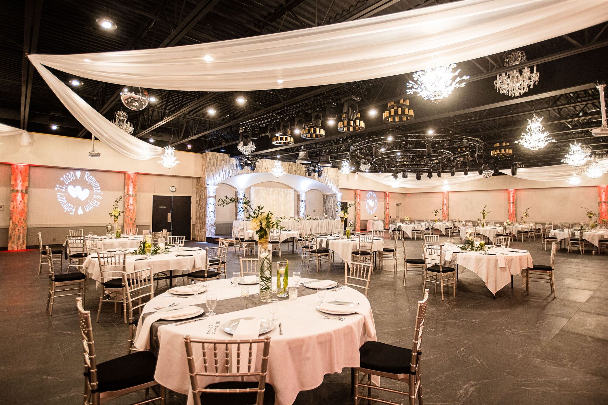 Ballroom set for a reception with blush linens, gold chiavari chairs, a monogram gobo, and warm uplighting at Royal Cliff, Eagan MN