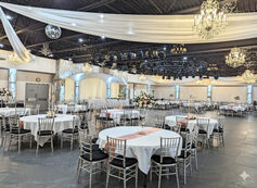 Wide view of the chandelier-lit ballroom with draped ceiling and rounds of tables ready for guests at Royal Cliff, Eagan MN