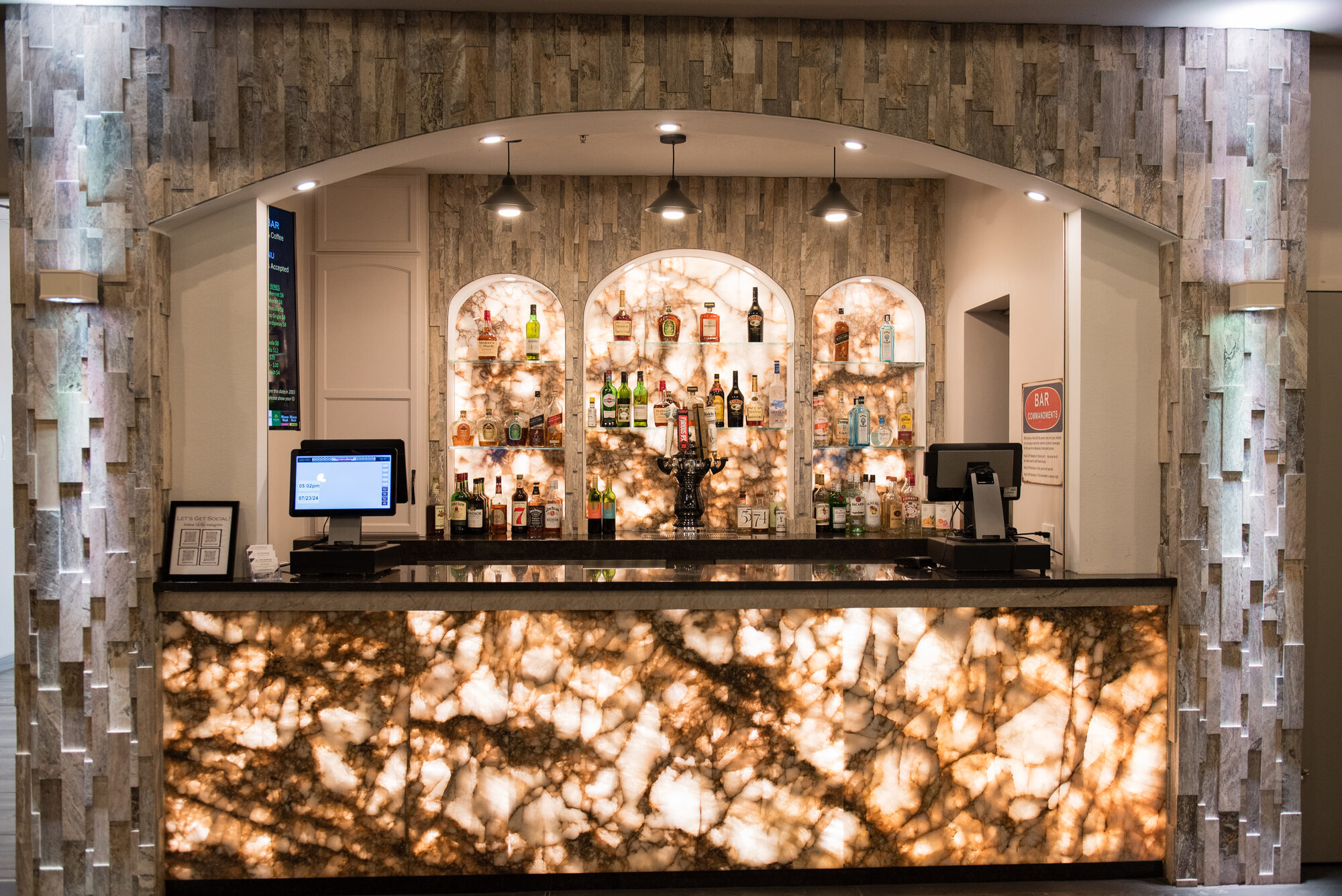 Backlit onyx bar with a glowing stone front and arched liquor displays pouring wine, beer, and cocktails at Royal Cliff, Eagan MN