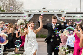 Bride and groom cheering as they walk out through a tunnel of guests blowing bubbles in the garden at Royal Cliff, Eagan MN
