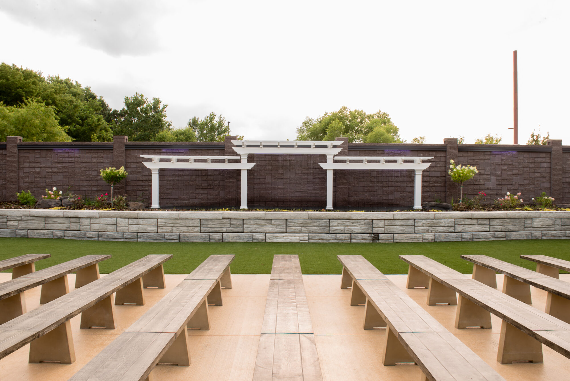 Outdoor ceremony amphitheater with wood benches facing the white pergolas and stone wall at Royal Cliff, Eagan MN
