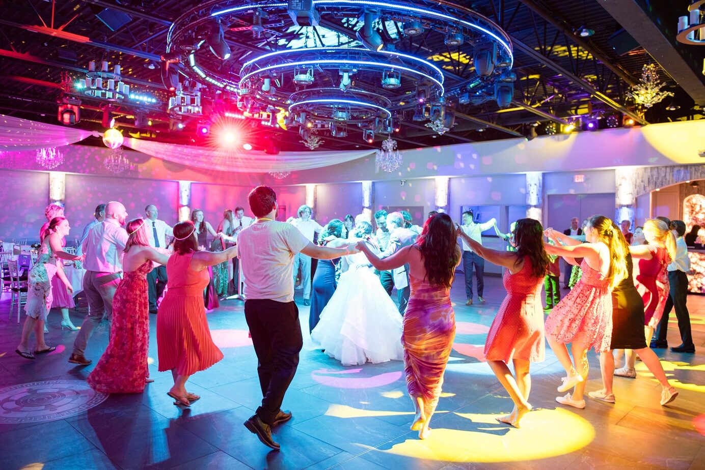 Guests dancing in a circle around the bride under colorful intelligent lighting and a disco ball at Royal Cliff, Eagan MN