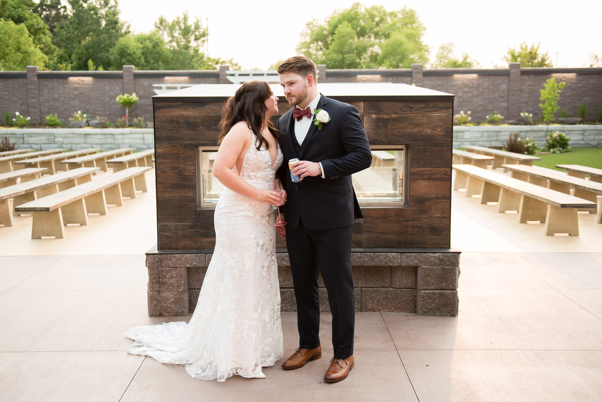 Bride and groom share a moment in front of the modern wood-clad outdoor fireplace with ceremony benches behind them at golden hour at Royal Cliff, Eagan MN