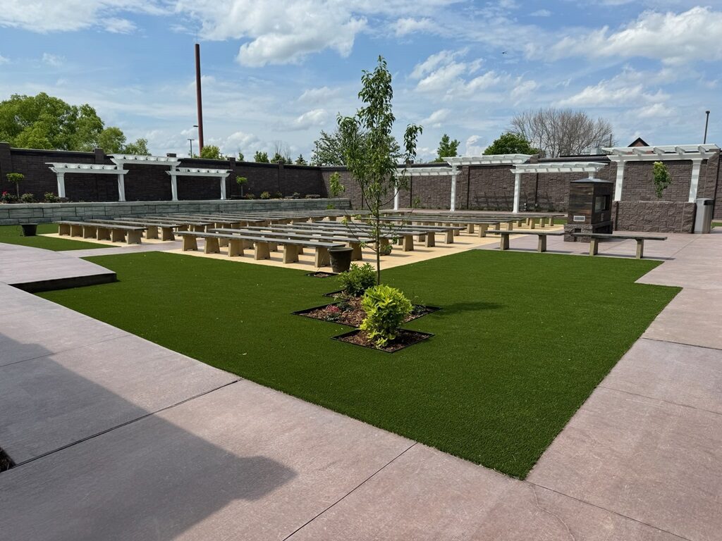 Outdoor ceremony garden set with stone benches, white pergolas, and a young tree under blue sky at Royal Cliff, Eagan MN
