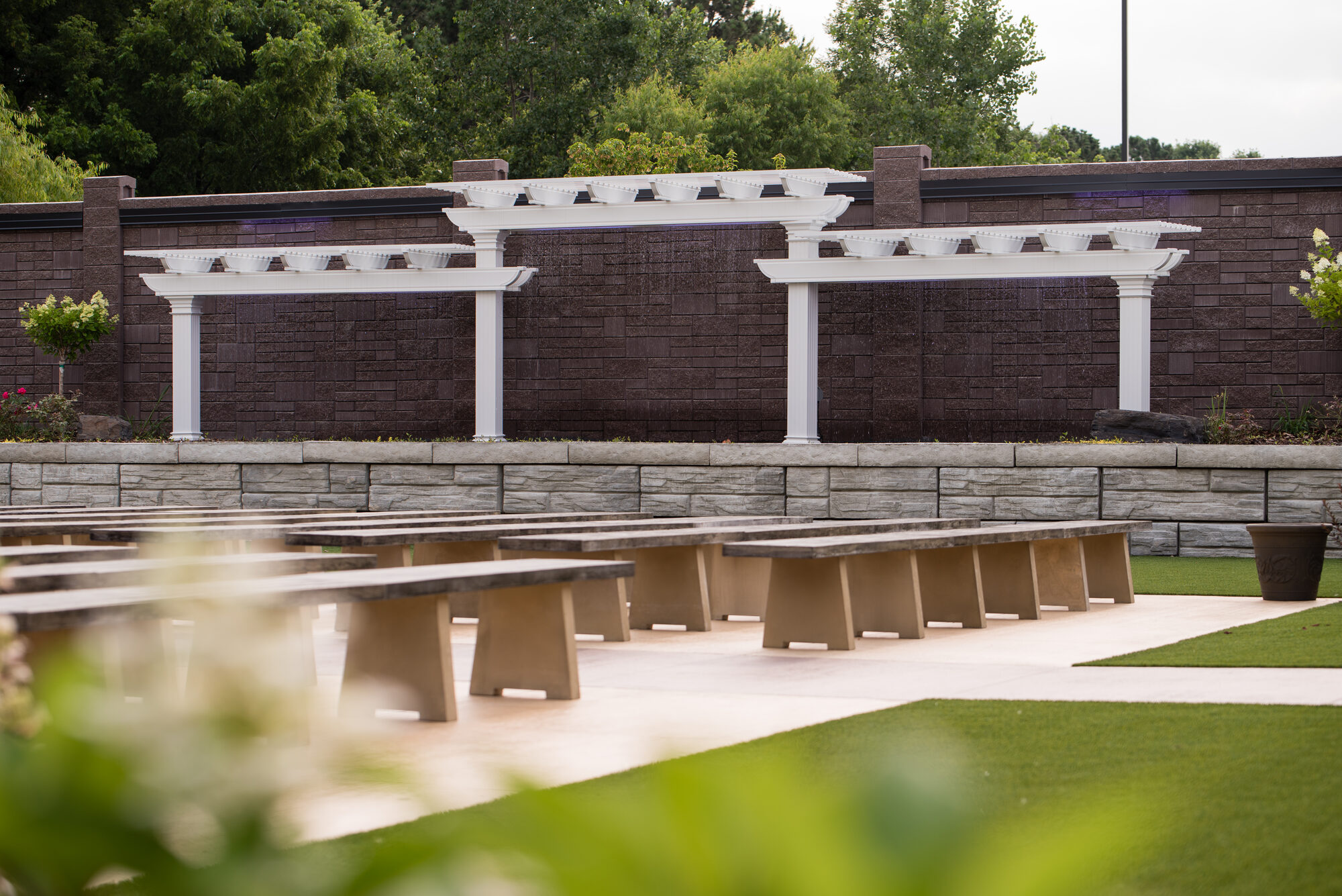 Wide view of the outdoor ceremony garden with wood benches facing three white pergolas along the stone wall at Royal Cliff, Eagan MN