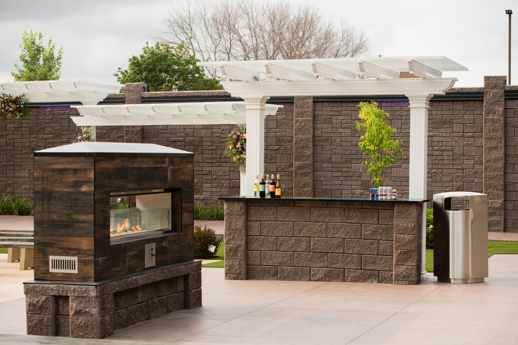 Outdoor stone bar topped with wine and drinks beside the modern linear fireplace and white pergolas in the garden at Royal Cliff, Eagan MN